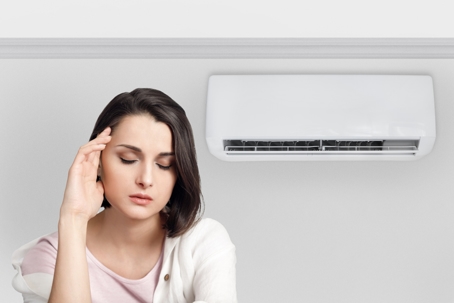 Woman holding her head while experiencing a cold and feeling unwell due to the air conditioner.